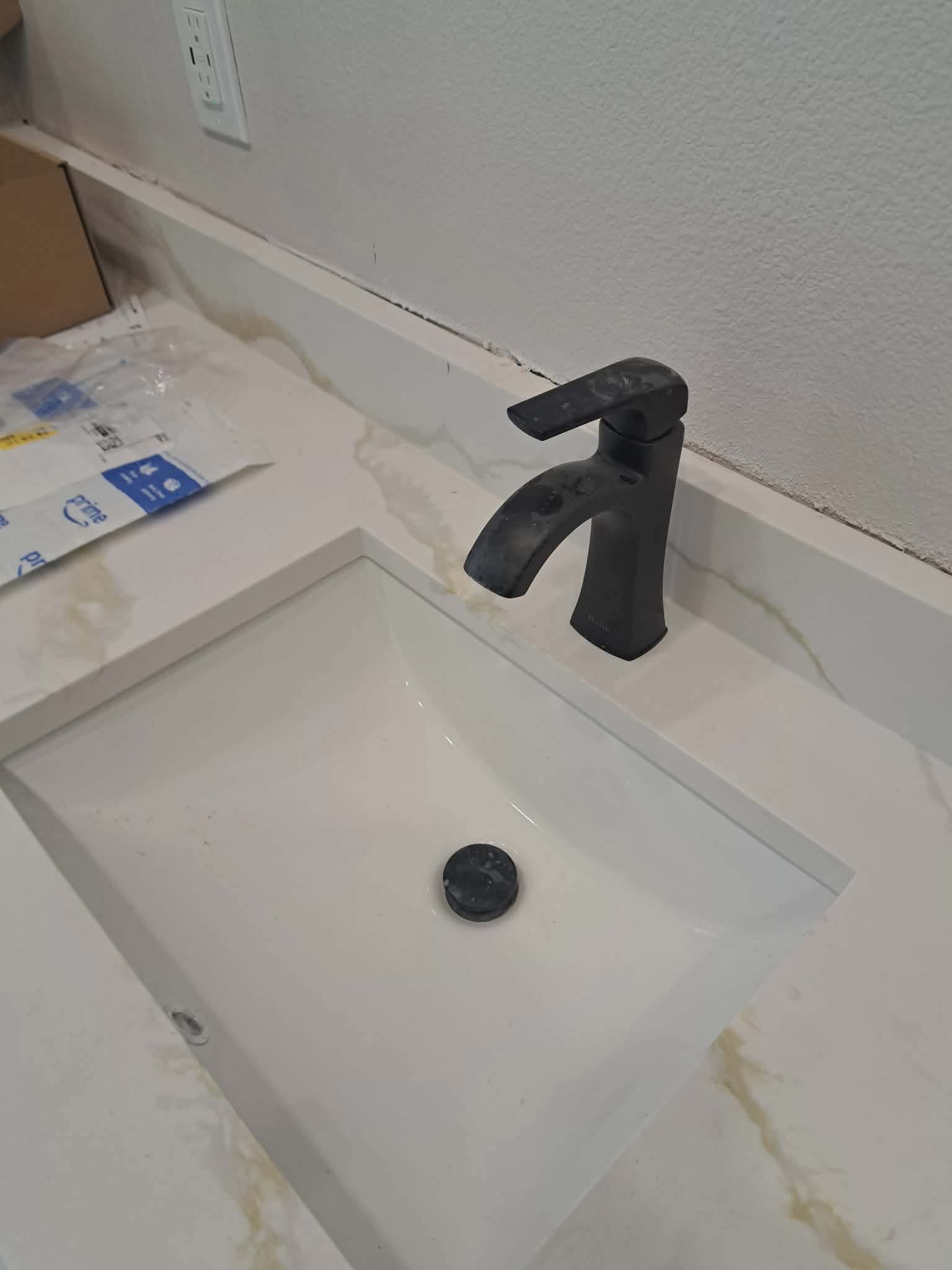 Modern black faucet on a white marble countertop above a rectangular white bathroom sink.