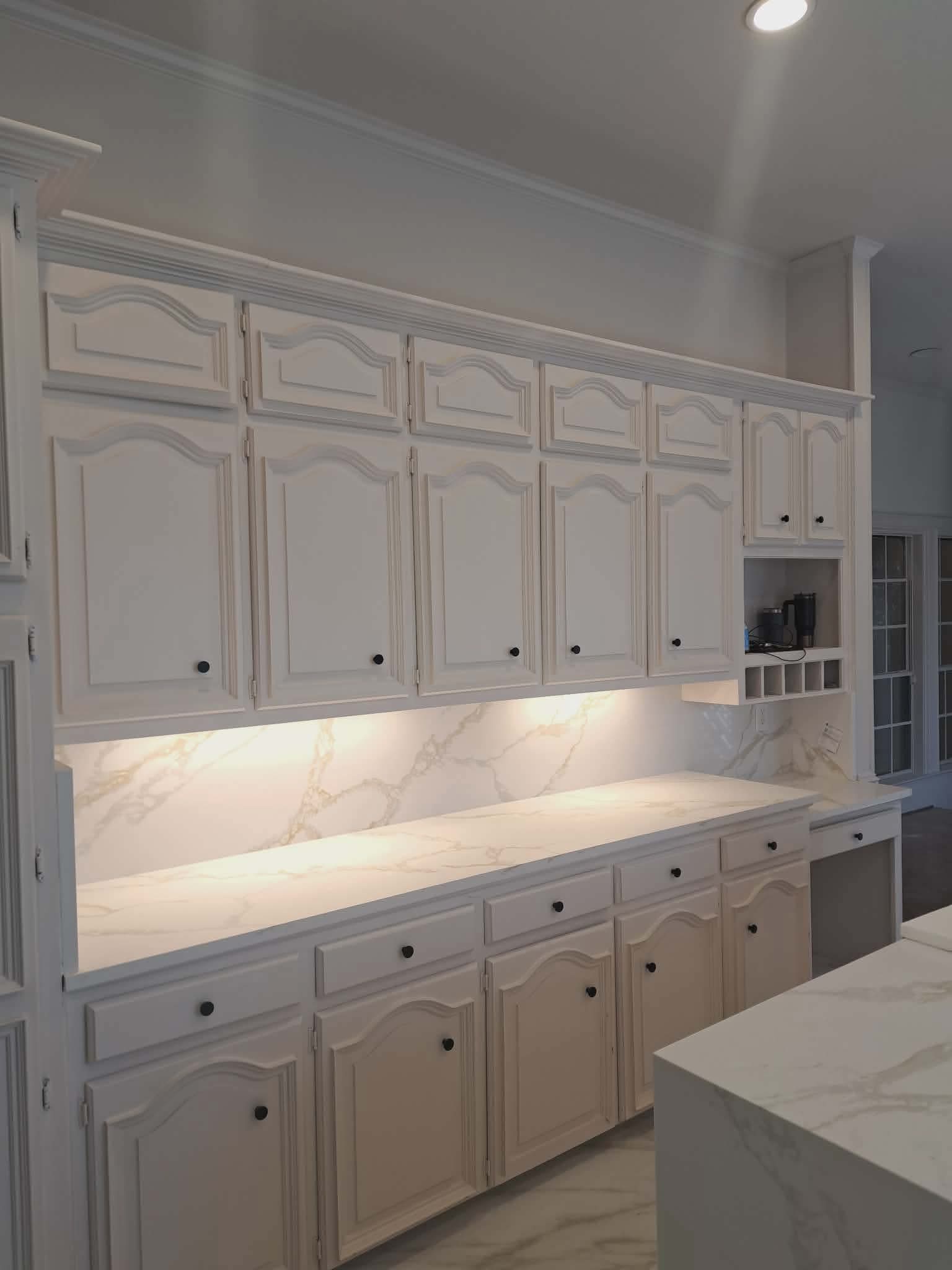Elegant white kitchen cabinets with arched panels, marble countertops, and warm under-cabinet lighting.