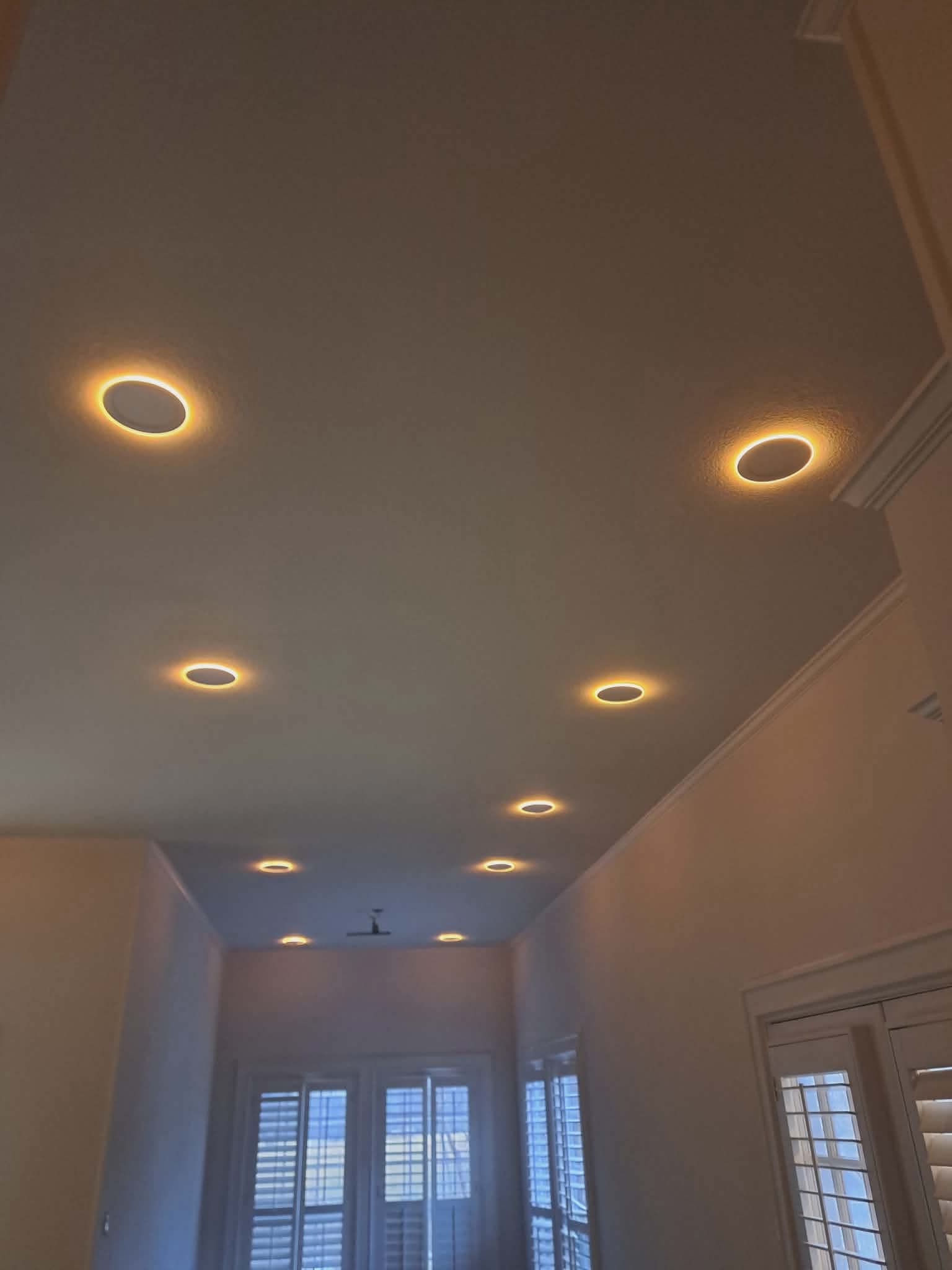 Warm circular recessed lights glow on a white ceiling above a hallway with shutters.