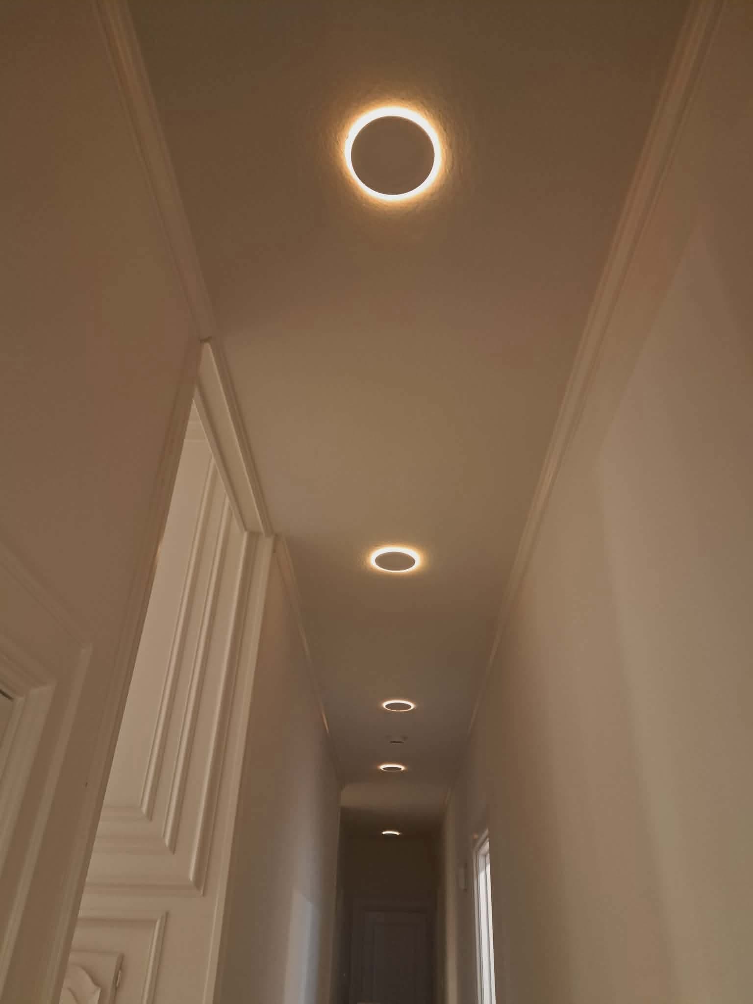 Glowing circular ring lights recessed into the ceiling of a long, narrow white hallway.