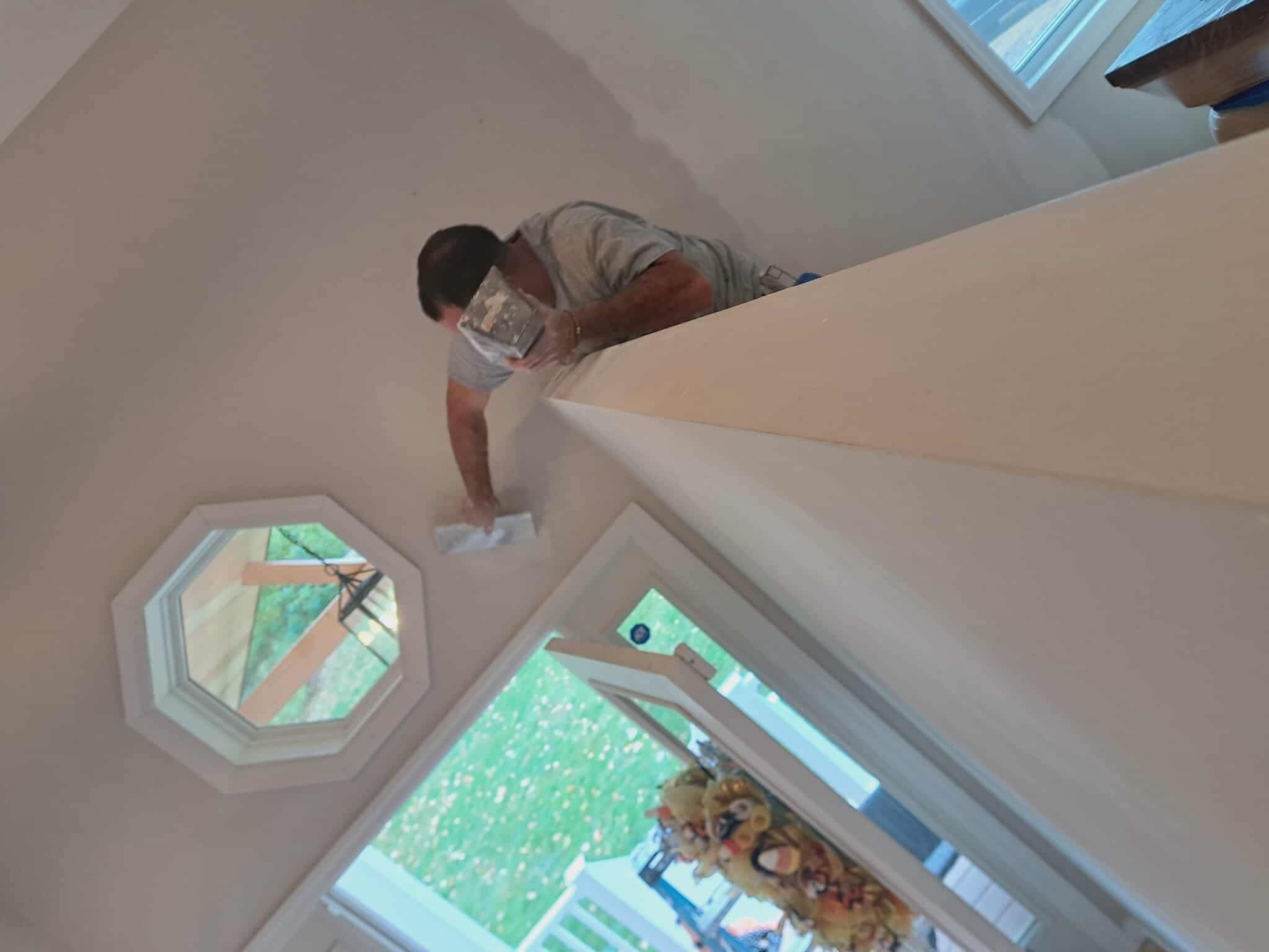 Man leaning over a ledge to apply joint compound near an octagonal window.