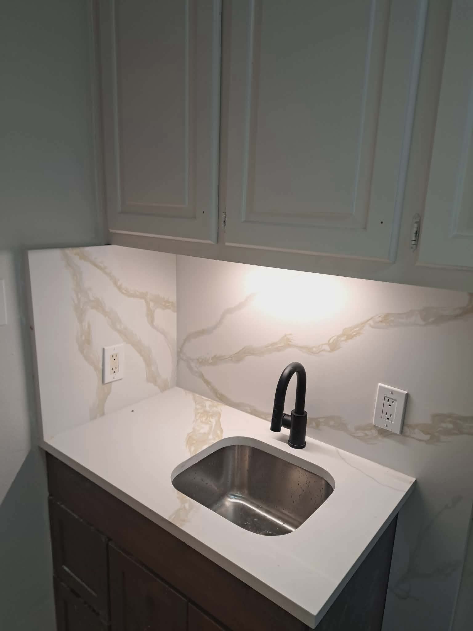 White marble-veined backsplash and countertop with a small stainless steel sink and black faucet.