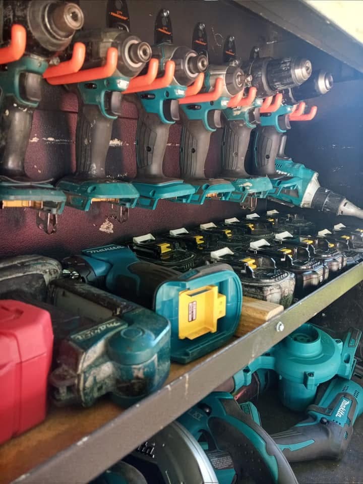 Teal power drills hanging on orange hooks above shelves filled with batteries and tools.