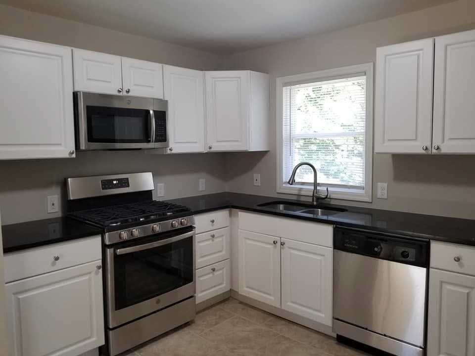 Modern kitchen featuring white cabinets, black countertops, stainless steel appliances, and a window with blinds.