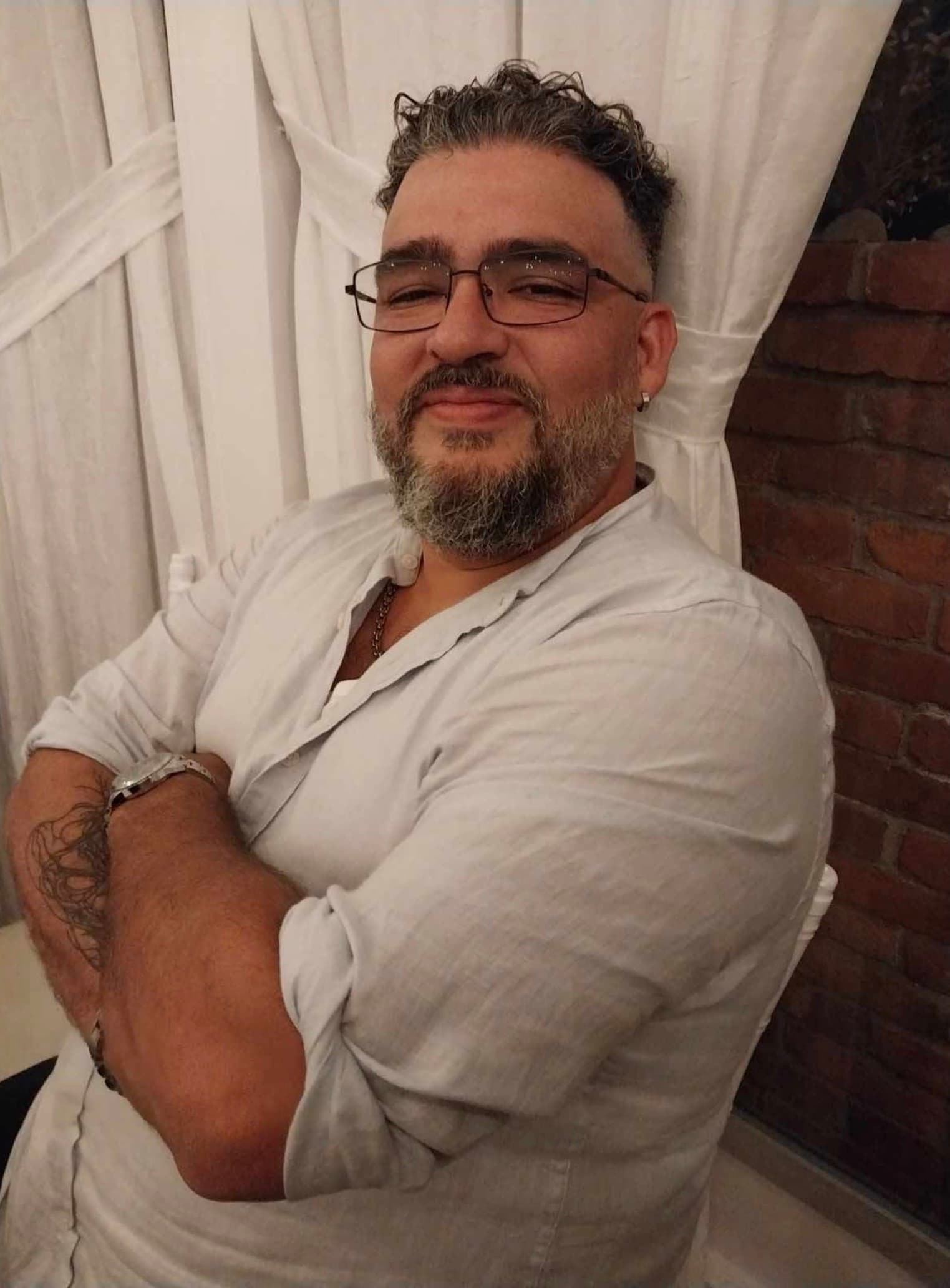 Middle-aged man with glasses and a salt-and-pepper beard, sitting with his arms crossed.