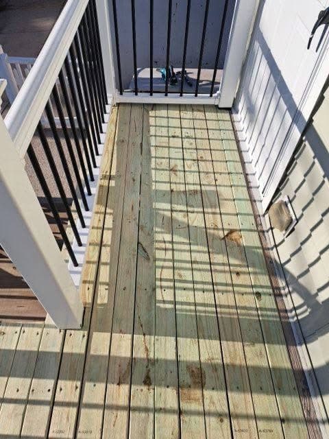 Freshly installed wooden deck boards on a balcony featuring white railings and black spindles.