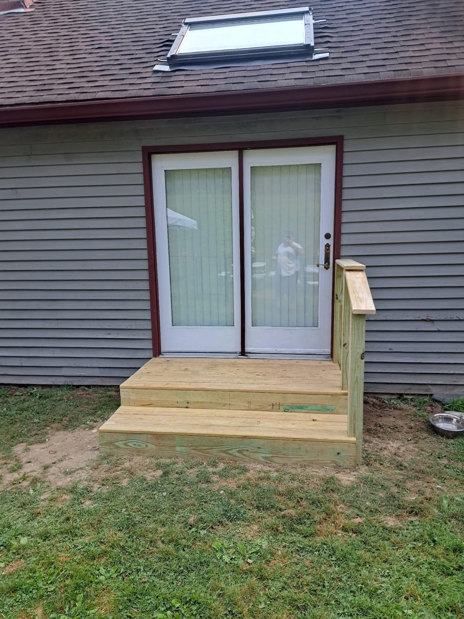 New wooden steps and railing lead to white French doors on a grey house.