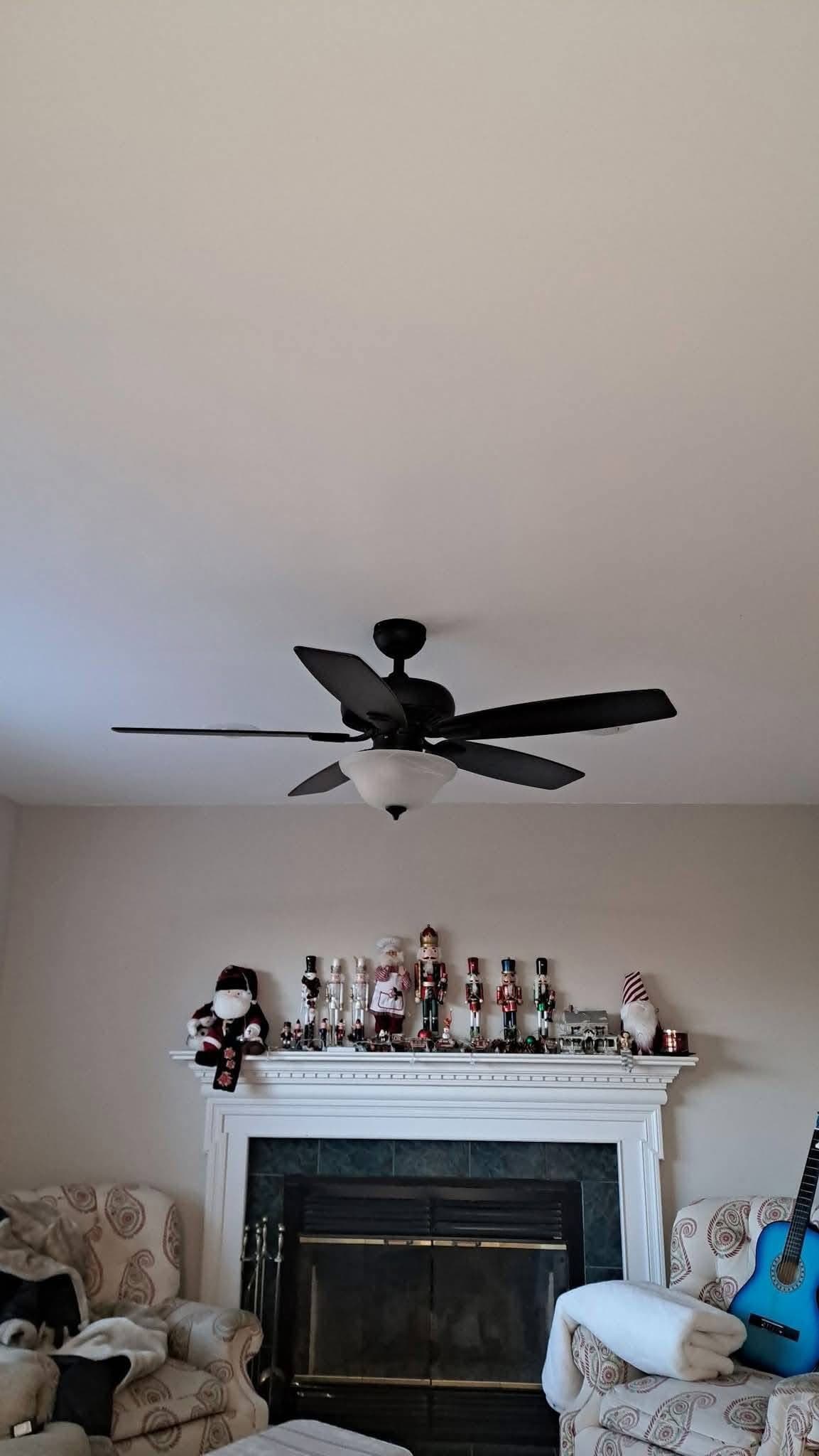 Black ceiling fan above a fireplace mantel decorated with nutcrackers, flanked by two patterned armchairs.