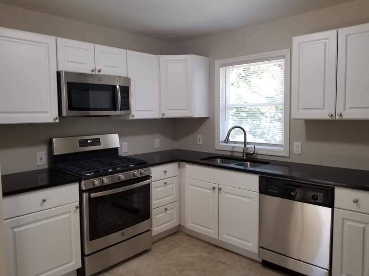 Modern kitchen with white cabinets, black countertops, stainless steel appliances, and a bright window.