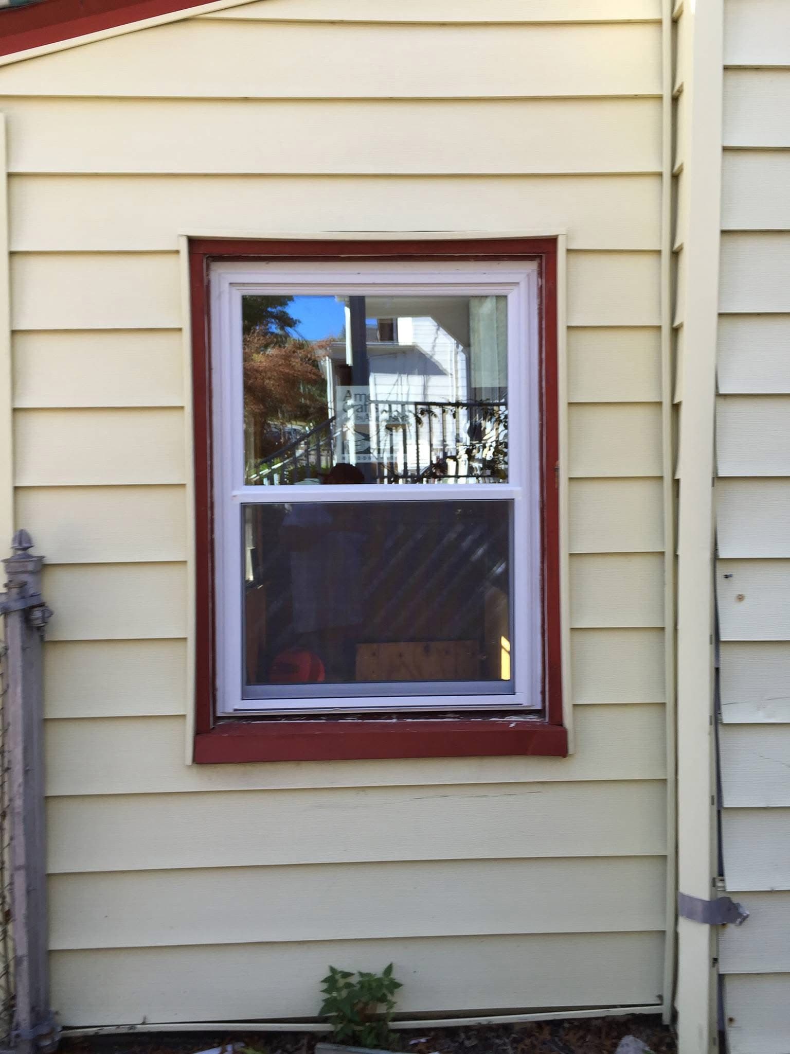White double-hung window with red trim on a house with light yellow horizontal siding.
